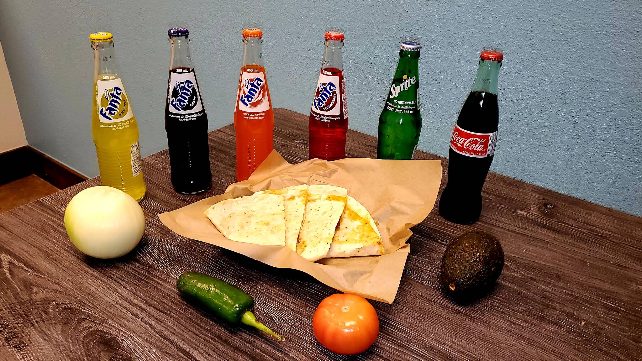 Cut quesadilla on paper with a jalapeño, a tomato, and an avocado on a wooden table