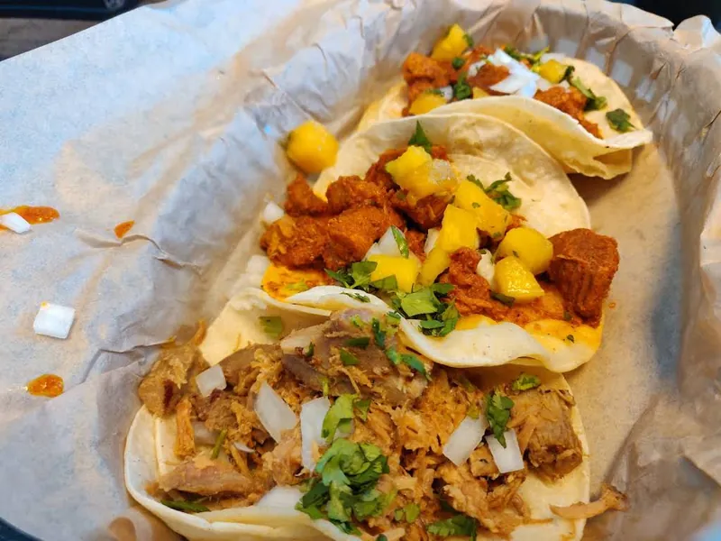Tacos on corn tortillas in a paper-lined basket with chopped toppings