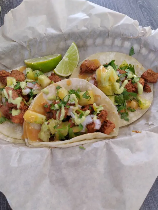 Tacos in a paper-lined basket with chopped toppings and lime wedges