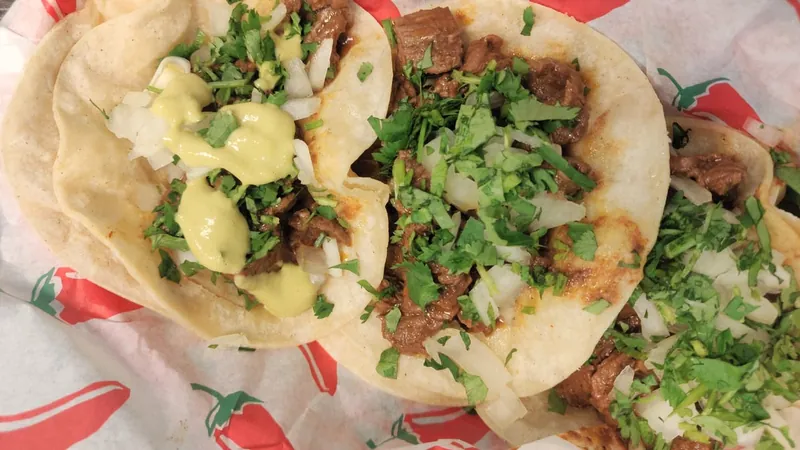 Close view of tacos on corn tortillas topped with chopped onion and cilantro