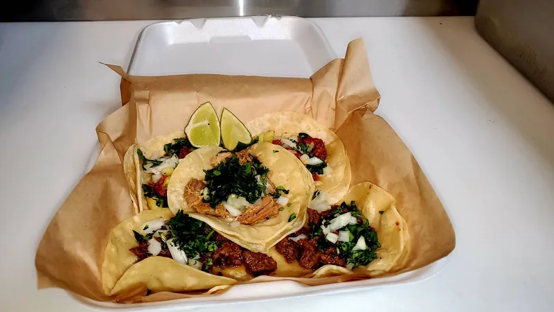 Tacos with lime wedges and chopped cilantro in a paper-lined takeout container